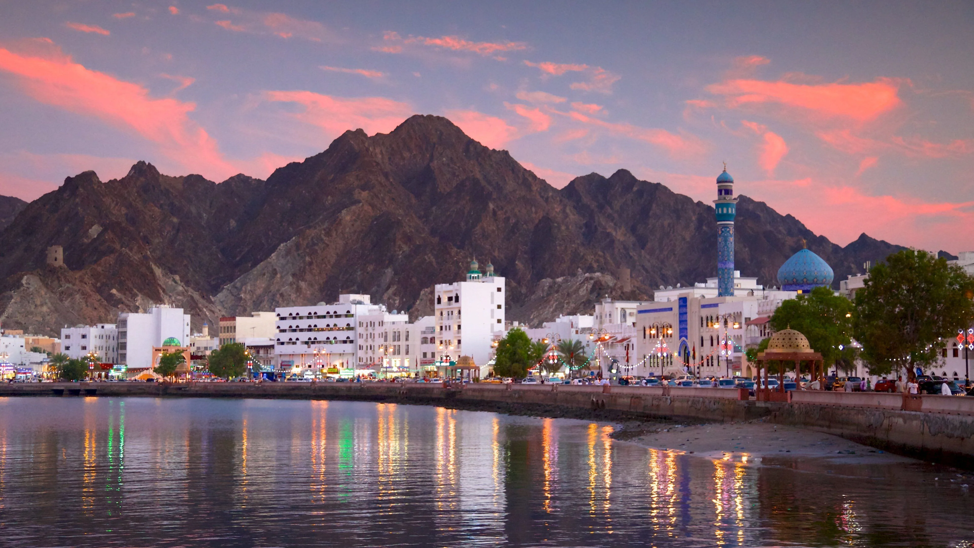 Muscat waterfront at dusk with mountains behind the city