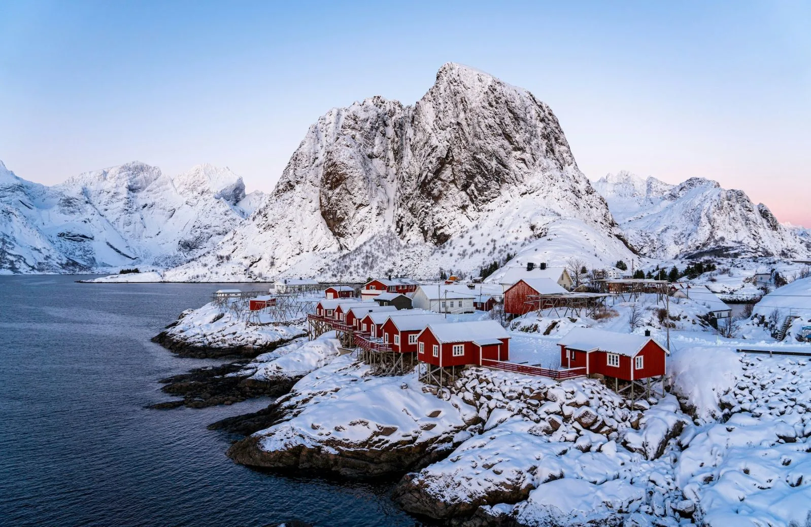 Snow-covered mountains and red cabins beside the water in Norway