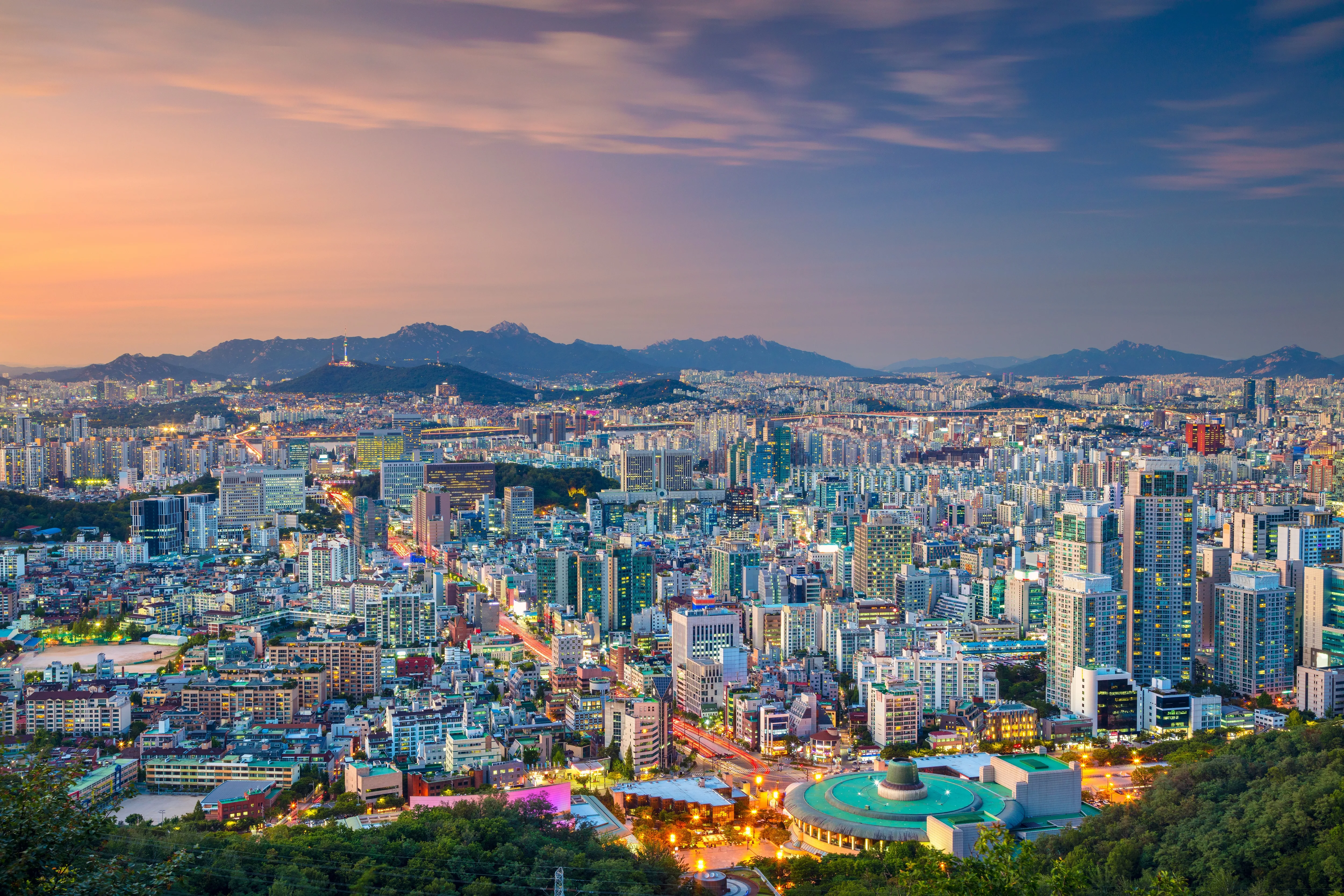 Seoul skyline at dusk with city lights and mountains beyond